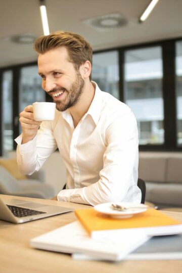 depth of field photo of man sitting on chair while holding cup in front of table